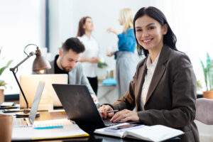 processo-de-contratacao-passo-a-passo-para-nao-errar. Imagem com uma mulher na mesa de trabalho, digitando no notebook e com um contrato ao lado.