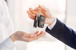 Imagem de representante da concessionária de veículos entregando as chaves de carro para o consumidor.