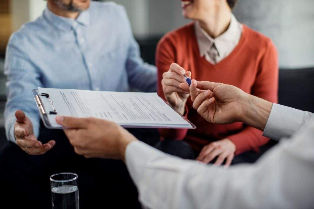 Imagem de casal e profissional com um contrato em prancheta, simbolizando o contrato de financiamento imobiliário.