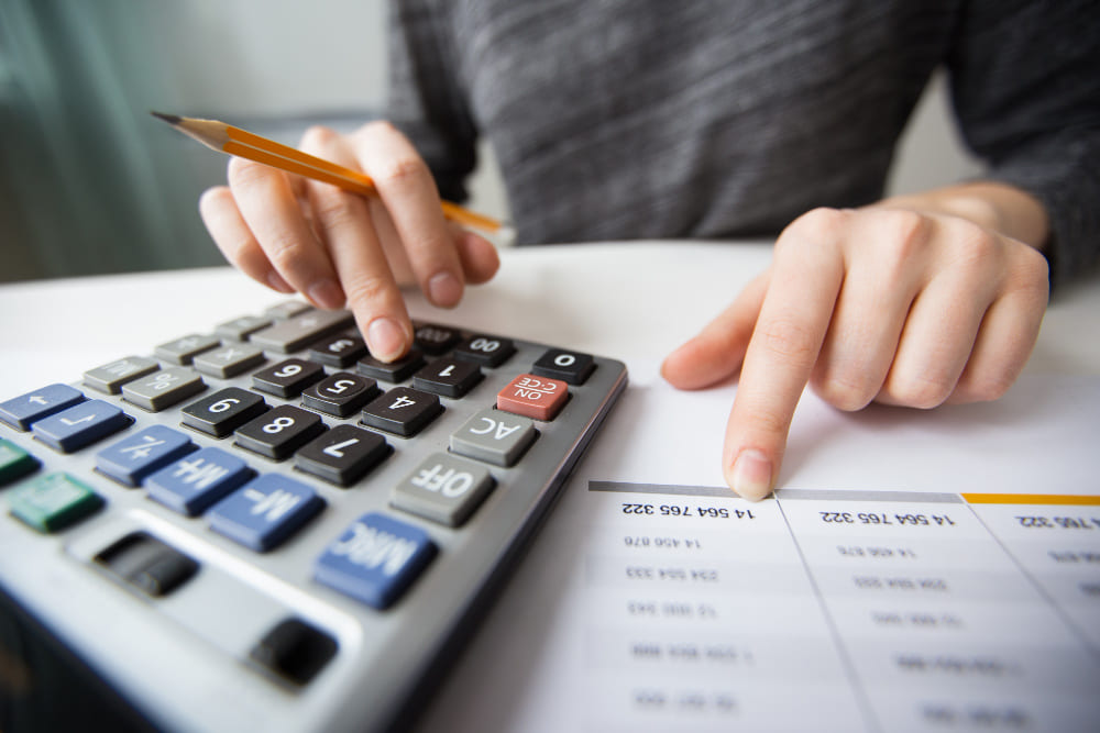 Imagem de mesa, com uma pessoa fazendo cálculos na calculadora e notebook, simbolizando a pensão por morte para filho incapaz.