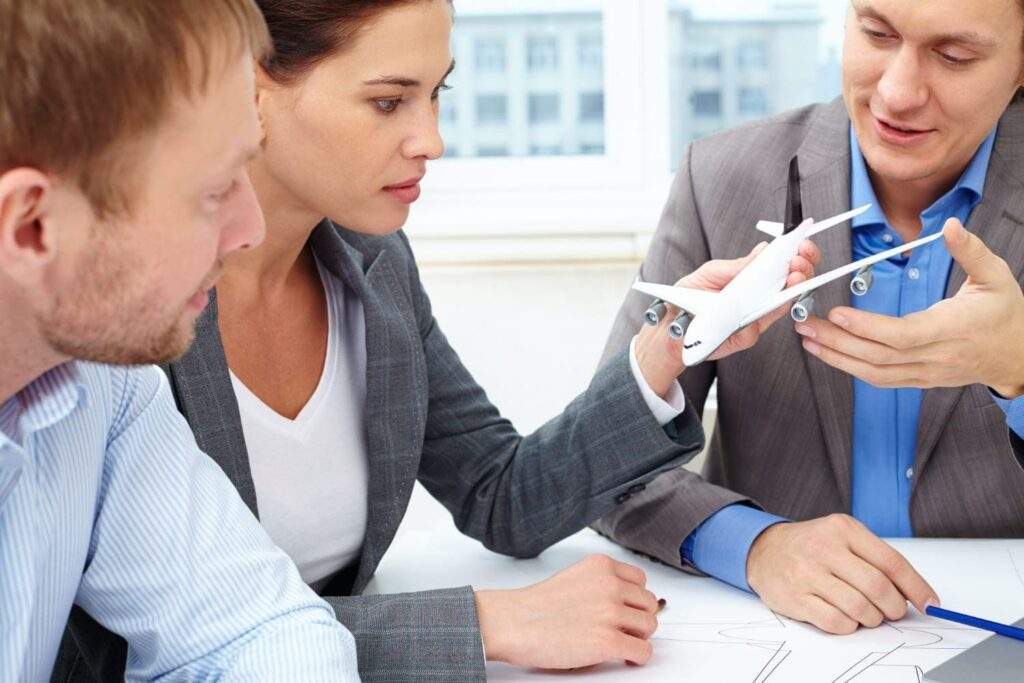 Imagem de três advogados sentados em uma mesa, segurando uma miniatura de avião, simbolizando um advogado especialista em companhias aéreas.