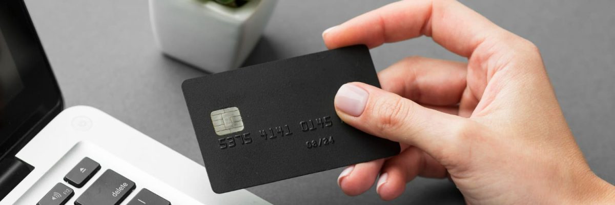 Imagem de pessoa com cartão na mão, perto do noteboook, representando o cartão de crédito clonado.