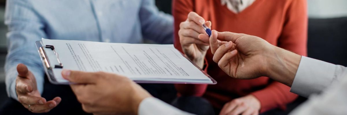 Imagem de casal e profissional com um contrato em prancheta, simbolizando o contrato de financiamento imobiliário.