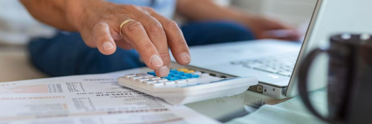 Imagem com pessoa fazendo cálculos na calculadora, notebook e contrato, simbolizando a revisão de dívidas bancárias.